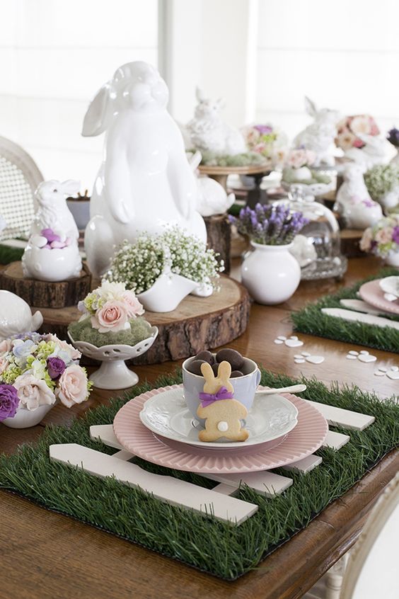 a fun Easter tablescape with bunnies, pastel flowers, a grass placemat, some cookies and candies is a cool idea