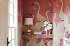 a glam pink powder room with pink swan mural walls, a pink marble shelf, white applainces and a chic table lamp