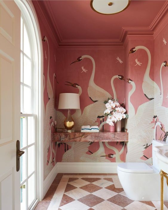 a glam pink powder room with pink swan mural walls, a pink marble shelf, white applainces and a chic table lamp