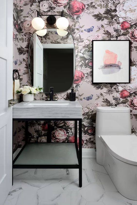 a glam powder room with bold floral wallpaper, a white console sink, a mirror of an oval shape and some blooms