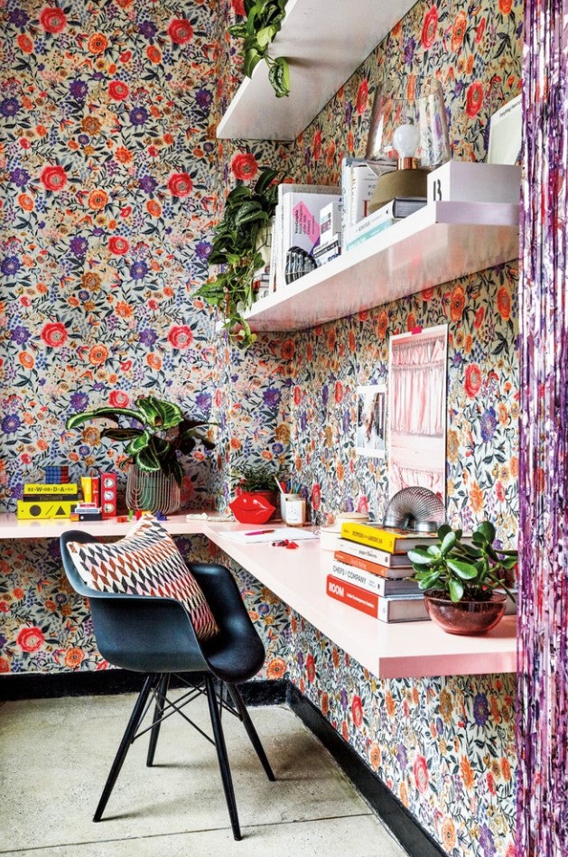 a jaw dropping home office nook covered with bright floral wallpaper, white floating shelves and a pink floating desk, lots of books and potted plants