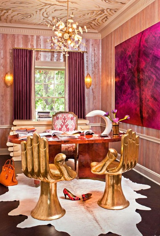 a jaw-dropping maximalist home office wiht a patterned ceiling, pink wallpaper, a stone desk, gold hand-shaped chairs, a statement artwork and curtains that echo with it