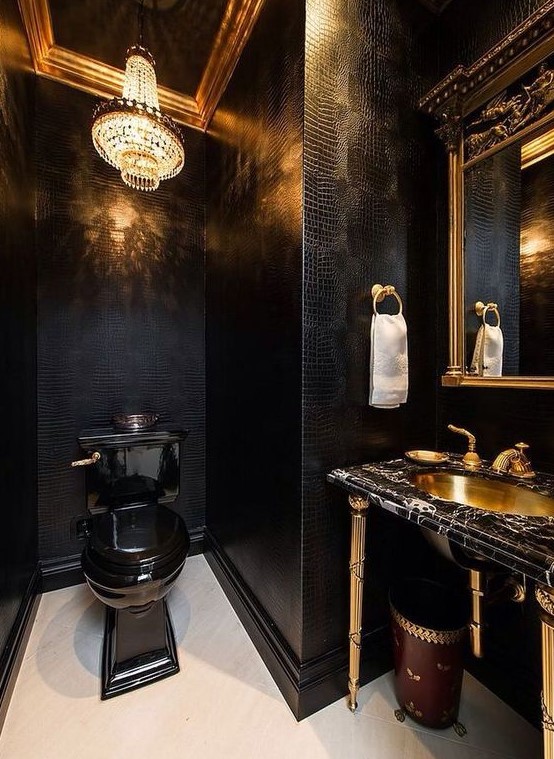 a luxurious powder room with black leather walls, a crystal chandelier, a black toilet, a black marble vanity and a gold sink