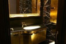 a luxurious powder room with black walls, chic gold touches, a gold vanity, some built-in lights and white appliances