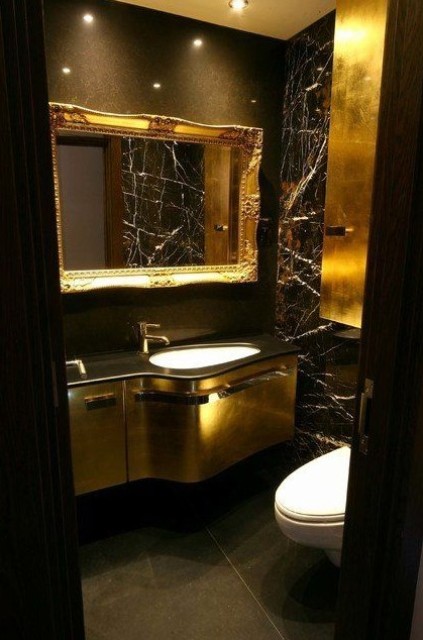 a luxurious powder room with black walls, chic gold touches, a gold vanity, some built-in lights and white appliances