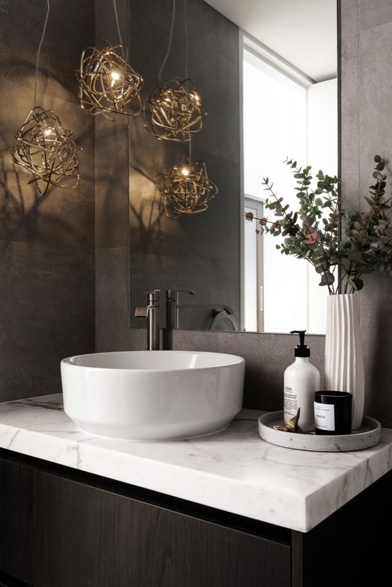 a luxurious powder room with cement tiles, a black vanity, a bowl sink and a white marble countertop, very catchy pendant lamps