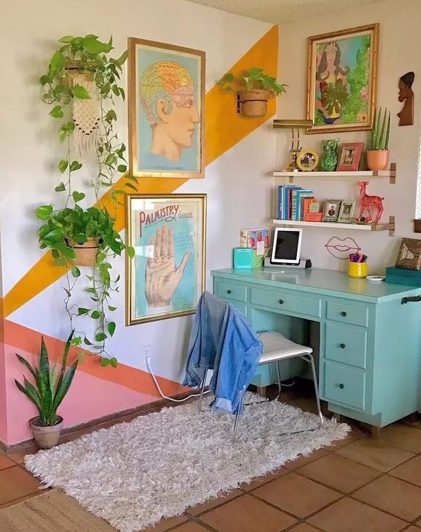 a maximalist home office with a color block accent wall, a turquoise desk, floating shelves, colorful art and lots of potted plants