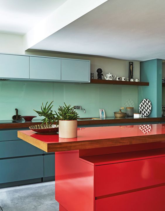 a minimalist kitchen with blue and muted blue cabinets, a mint green backsplash, a bold red kitchen island and wooden countertops