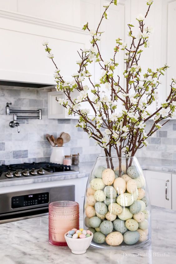 a modern Easter centerpiece of a large vase with pastel eggs and blooming branches is amazing