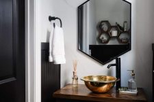a modern powder room with a black vanity, a hexagon mirror, a gold bowl sink and black fixtures is amazing