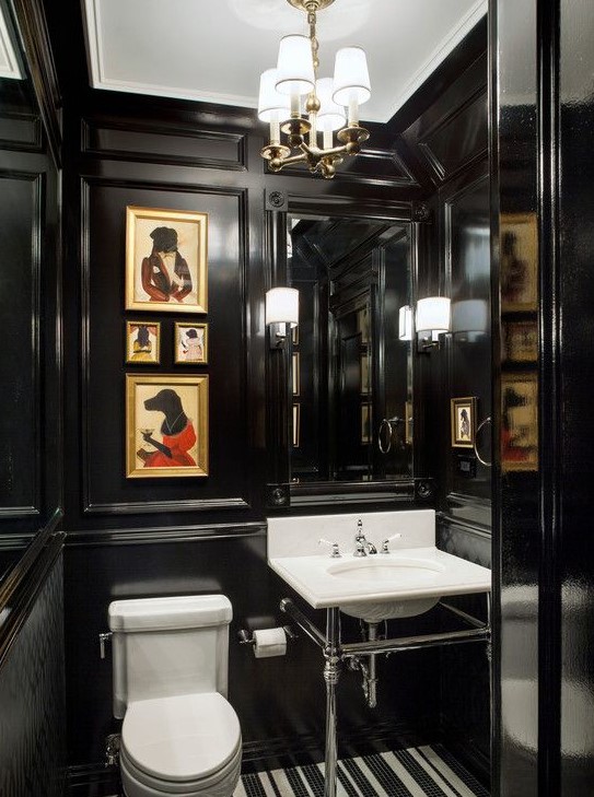 a moody and elegant powder room with black paneling, a built in mirror, a console sink, a white toilet and a mini gallery wall in bold colors