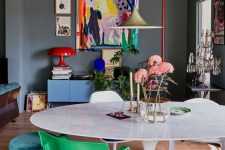 a moody home office made bright with furniture and artwork, with green and blue chairs and stools, a blue dresser, a colorful artwork and a red lamp is a lovely space