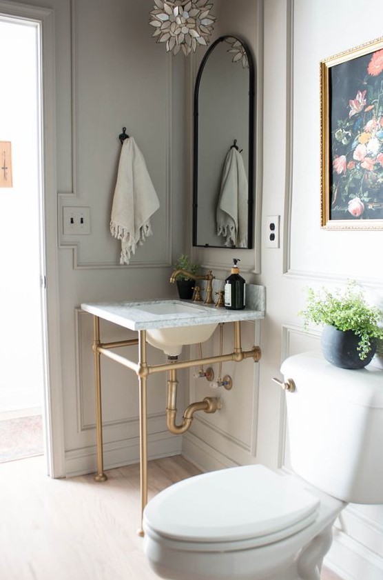 a neutral vintage powder room with grey paneled walls, a console sink, an arched mirror, white appliances and a pretty artwork