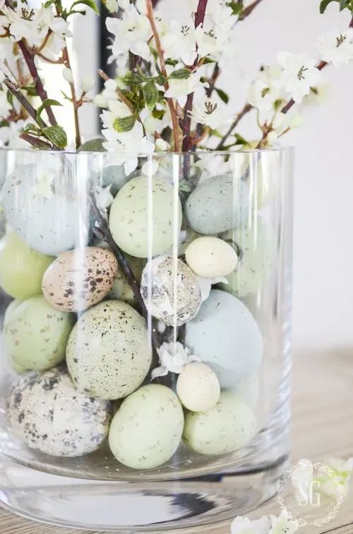 a pastel Easter centerpiece of a clear vase with pastel speckled eggs and blooming branches is a cool and catchy decoration