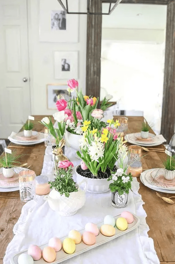 a pastel Easter table setting with potted greenery and blooms, candles, greenery in egg shells and pastel eggs