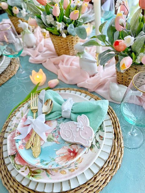 a pastel Easter table setting with turquoise linens, bright printed plates, gold cutlery, pastel tulips and candles