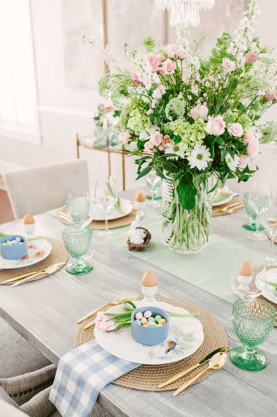 a pastel Easter tablescape with a pink floral centerpiece, blue and green linens, green glasses and blue cups with candies plus eggs