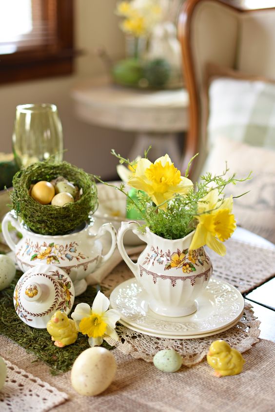 a pretty Easter centerpiece of some greenery and yellow blooms, a moss nest with eggs and some chicks and blooms on the table