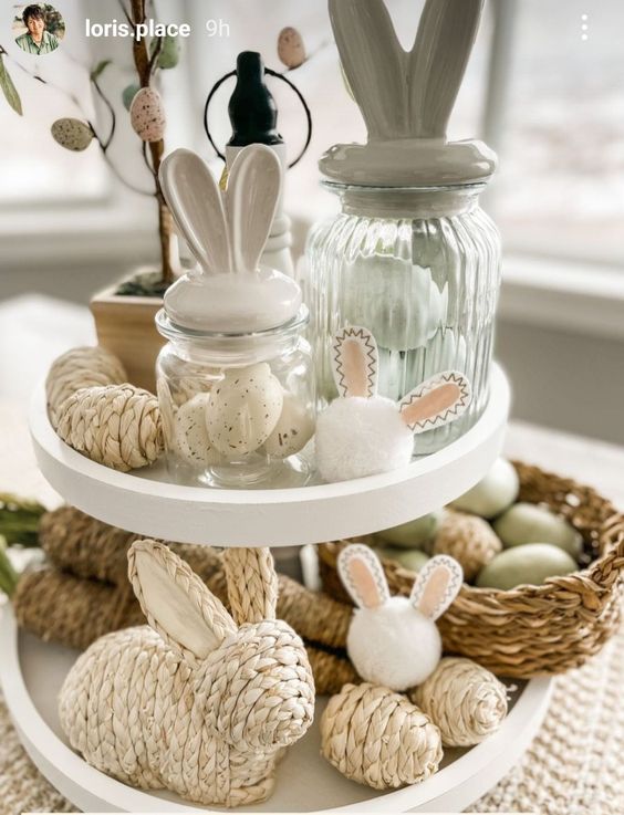 a pretty Easter decoration of a tiered stand with jute bunnies and eggs, baskets with eggs and jars with bunnye ear lids