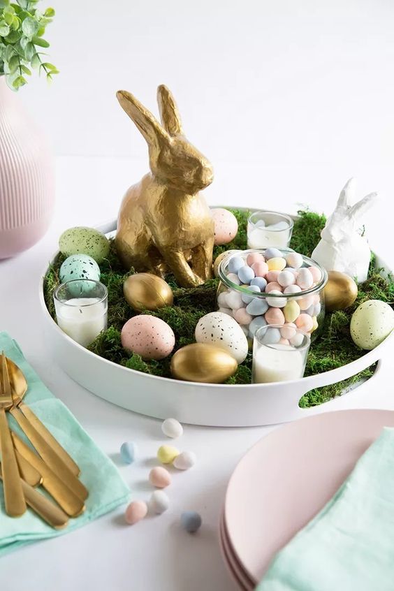 a pretty and simple Easter centerpiece of a tray with moss, pastel speckled eggs and pastel eggs in a jar, candles and bunnies