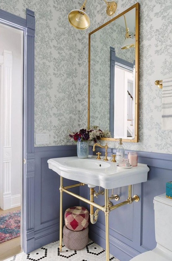 a pretty powder room with floral wallpaper, blue panels, a console sink, a mirror in a gilded frame, sconces and white appliances