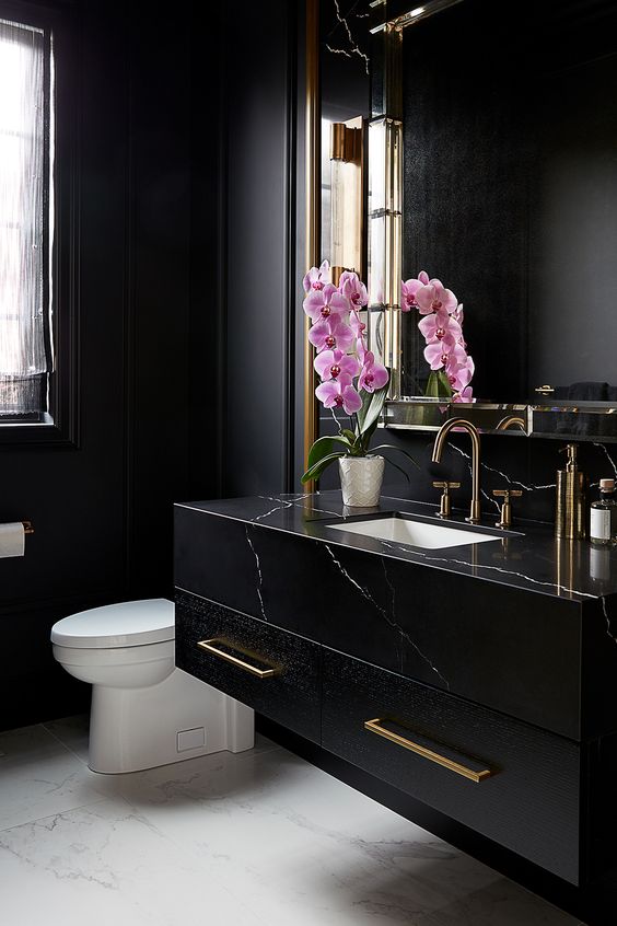 a refined black powder room with matte walls, a black marble vanity, a large mirror, white appliances and pink orchids