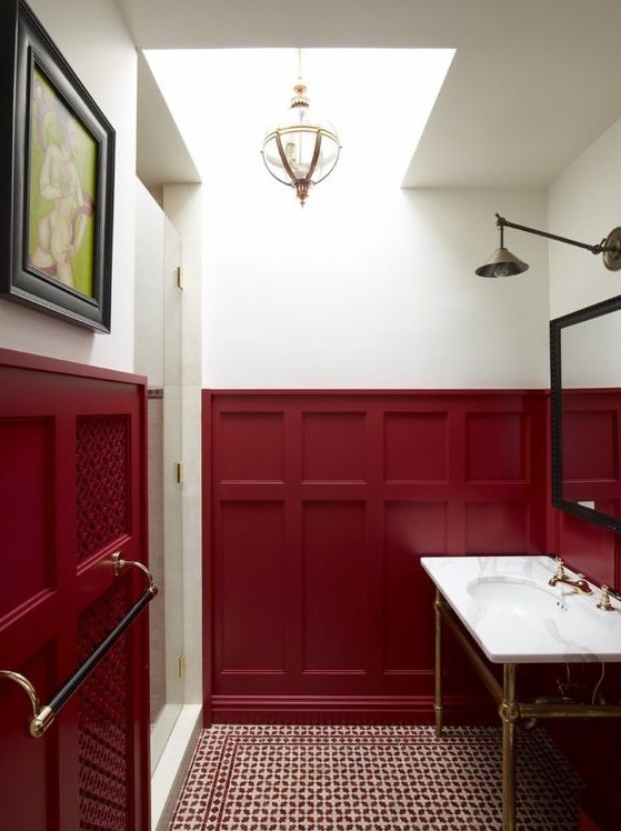 a refined powder room with burgundy wainscoting, a white sink, a large mirror, pendant and wall lamps