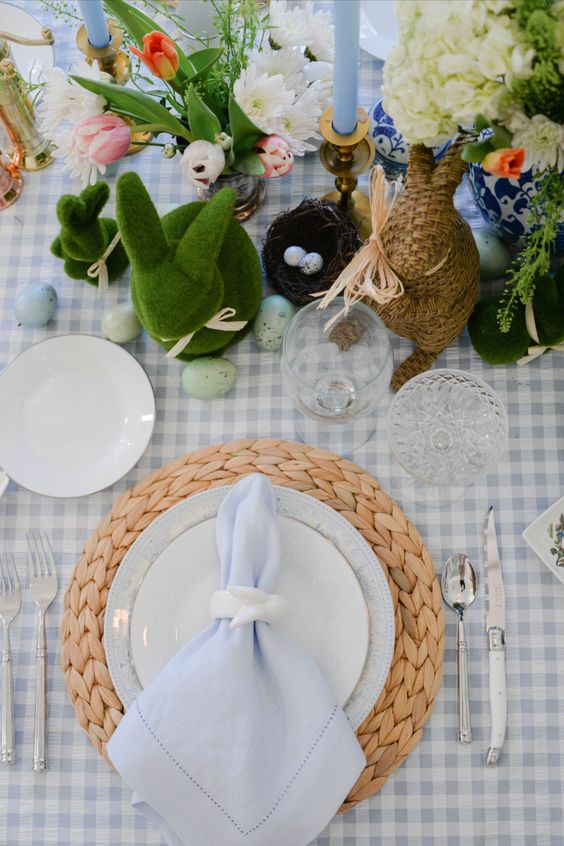 a rustic Easter table setting with a plaid tablecloth and serenity blue napkins, fresh flowers and various bunny figurines plus eggs