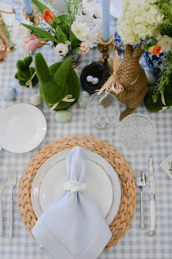 a rustic Easter table setting with a plaid tablecloth and serenity blue napkins, fresh flowers and various bunny figurines plus eggs