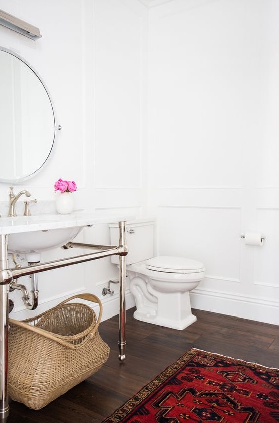 a serene powder room in white, with a dark floor, a bold rug, a console sink, a round mirror and white appliances is a cool idea