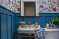a small and colorful powder room with floral wallpaper, blue panels, a console sink, white appliances, a catchy mirror and a basket with toilet paper