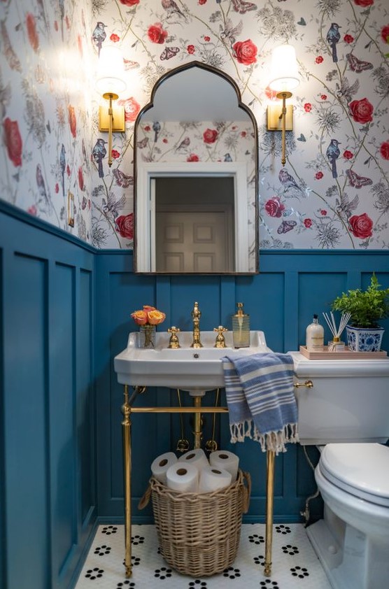 a small and colorful powder room with floral wallpaper, blue panels, a console sink, white appliances, a catchy mirror and a basket with toilet paper