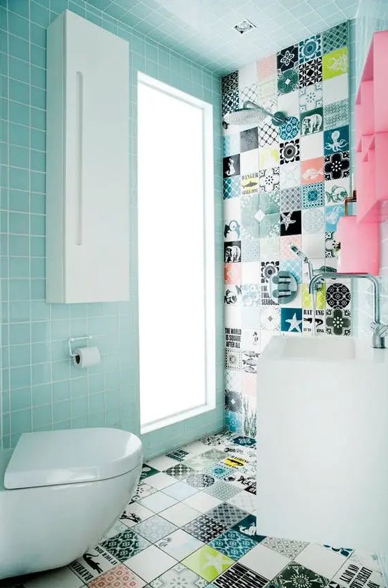 a small and cool powder room clad with light blue and printed tiles, with a pink storage unit and white appliances