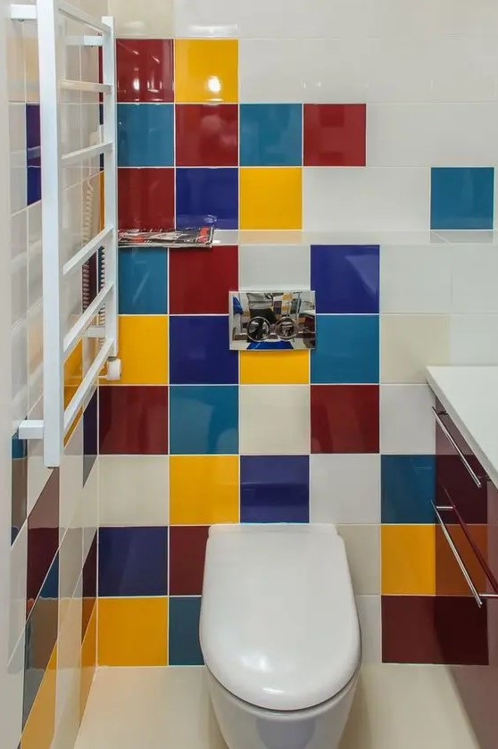 a small powder room clad with multi-color tiles of jewel tones, with a burgundy vanity and white appliances is super stylish and laconic