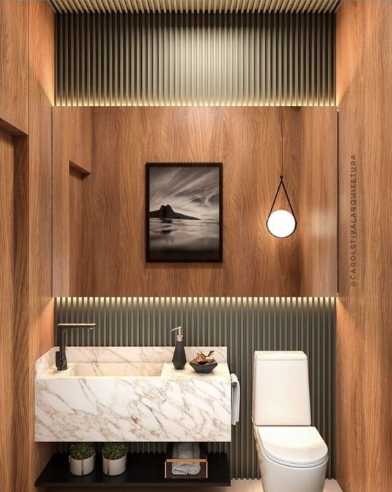 a small powder room clad with plywood and green panels, with a floating stone sink, a cool pendant lamp and an open shelf for storage