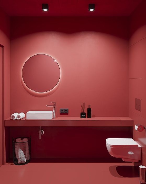 a sophisticated red minimalist powder room with matte walls, a floating vanity, a round lit up mirror, white appliances and ceiling lamps