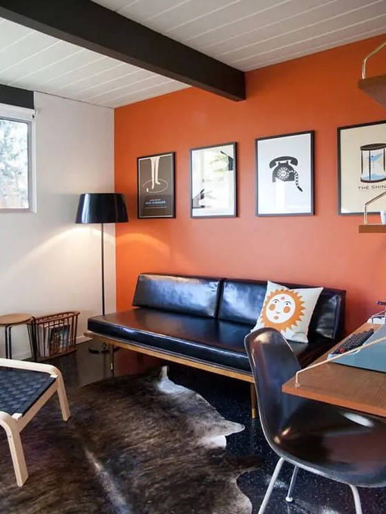 a stylish orange home office with a dark wooden beam, a black leather daybed, black chairs, a cool desk and layered rugs plus a gallery wall