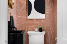 a super bold and chic powder room with pink printed wallpaper, a black floating sink, a white toilet, a black and white artwork