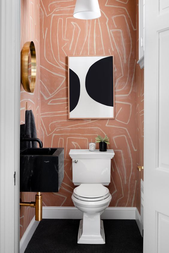 a super bold and chic powder room with pink printed wallpaper, a black floating sink, a white toilet, a black and white artwork