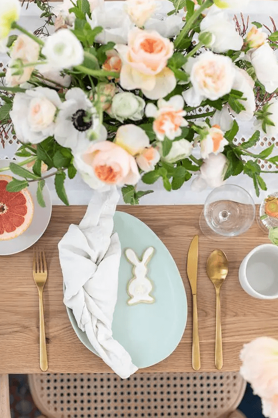 an Easter table setting with pastel blooms, a mint-colored egg-shaped plate, gold cutlery and bunny cookies