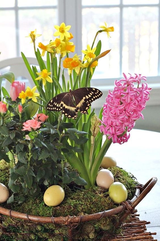 an adorable Easter centerpiece of moss, pastel eggs, greenery, pink and yellow blooms and a faux butterfly is adorable