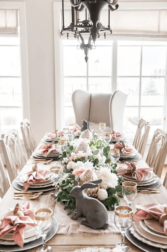 an elegant Easter tablescape with pink napkins, pink and white blooms and greenery, bunny figurines and gold rimmed glasses