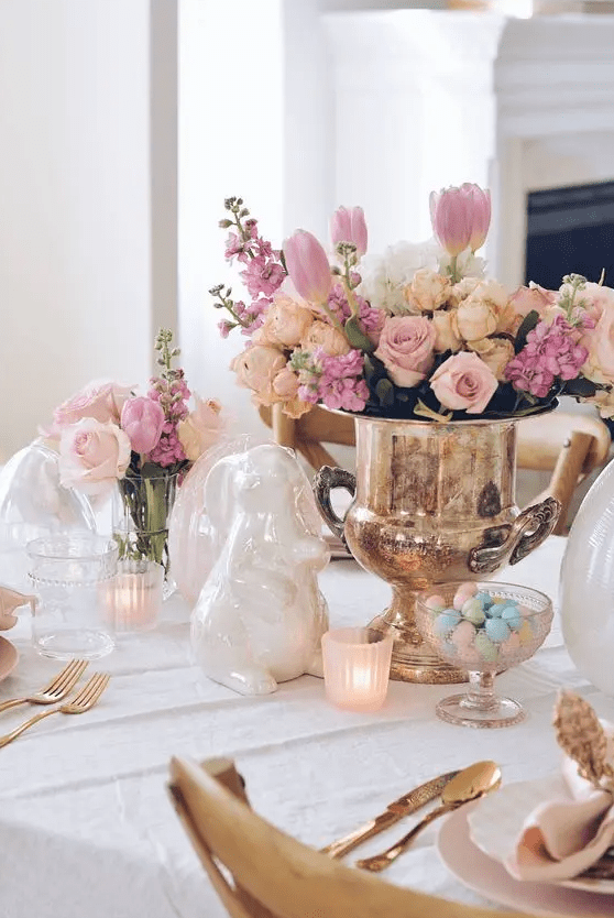 an elegant and chic Easter table setting with a lovely floral centerpiece, candles, porcelain bunnies, gold cutlery and pastel candies