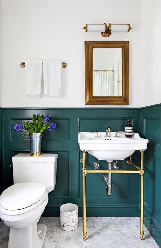 an elegant powder room with teal panels on the walls, a console sink, a mirror in a brass frame, white appliances and neutral towels
