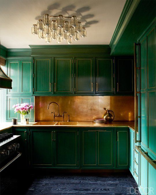 an emerald kitchen with a gold backsplash and countertops and a refined and chic chandelier is elegant and vintage-like