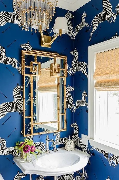 bold blue wallpaper with a zebra print and a gilded frame mirror makes up the whole look of this space