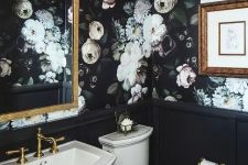 moody realistic floral wallpaper gives a tone to this vintage powder room, and there’s a gilded mirror and black paneling