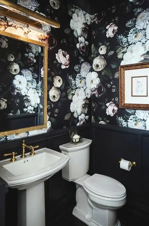 moody realistic floral wallpaper gives a tone to this vintage powder room, and there's a gilded mirror and black paneling