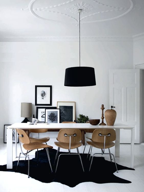 a beautiful Nordic dining room with a white table, plywood chairs, a gallery wall, a black pendant lamp and a black rug