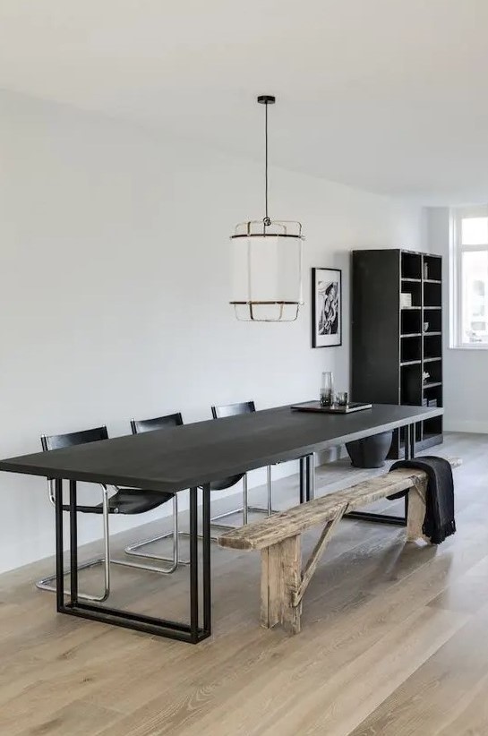 a catchy contemporary dining room with a black table, black leather chairs, a rustic wooden bench and a pendant lamp